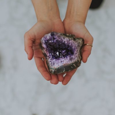 Hands holding a purple crystal geode for crystal healing on a white surface